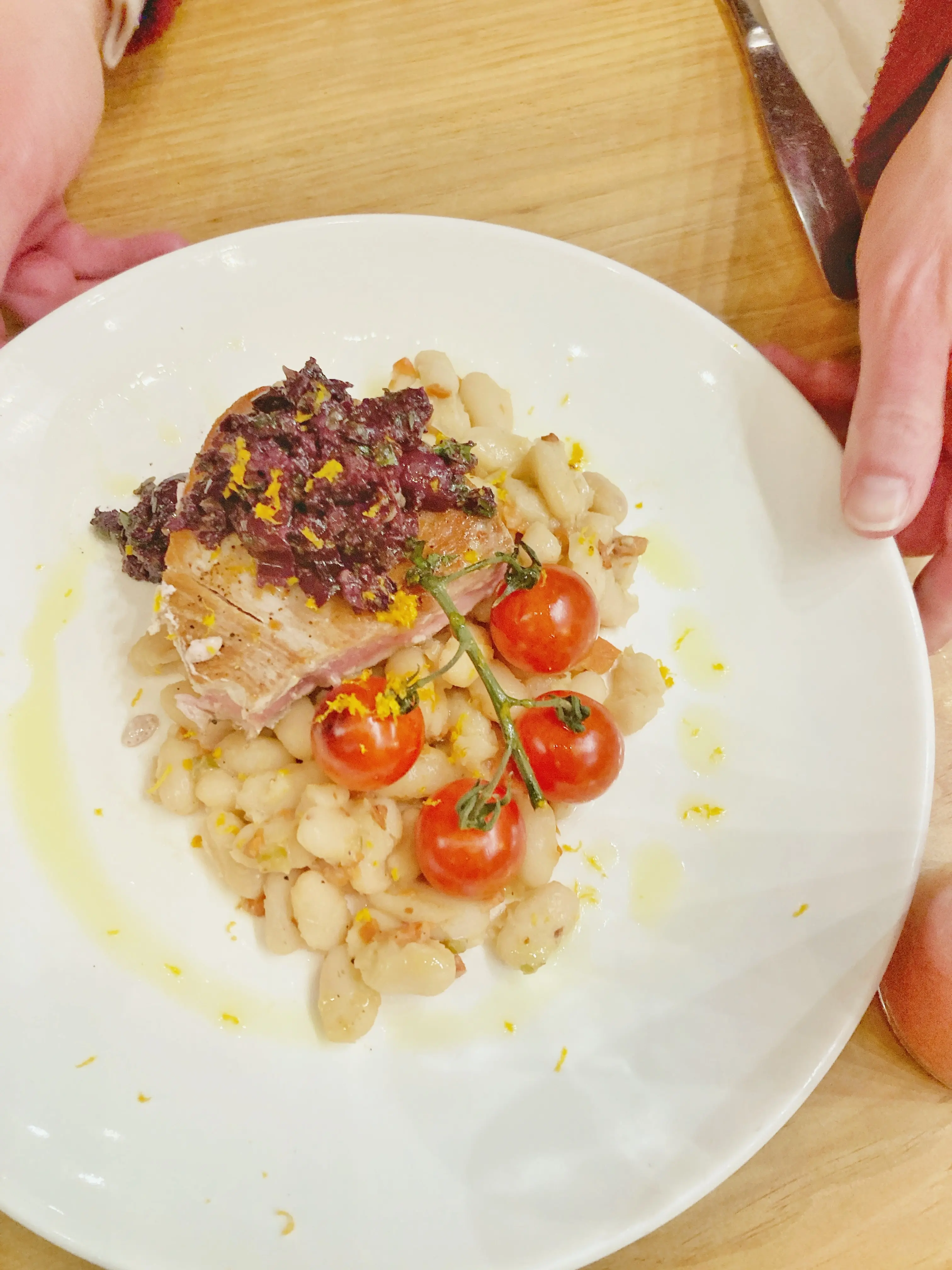 A person holds a plate with seared ahi tuna, white beans, roasted tomatoes, olive tapenade and orange zest at Duke's Dining Hall